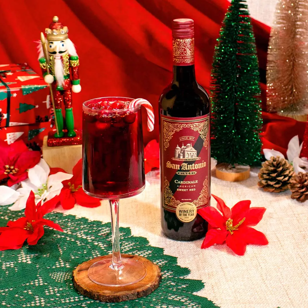 Bottle of San Antonio Winery Cardinale with a festive holiday drink, surrounded by Christmas decorations including a nutcracker and poinsettias.
