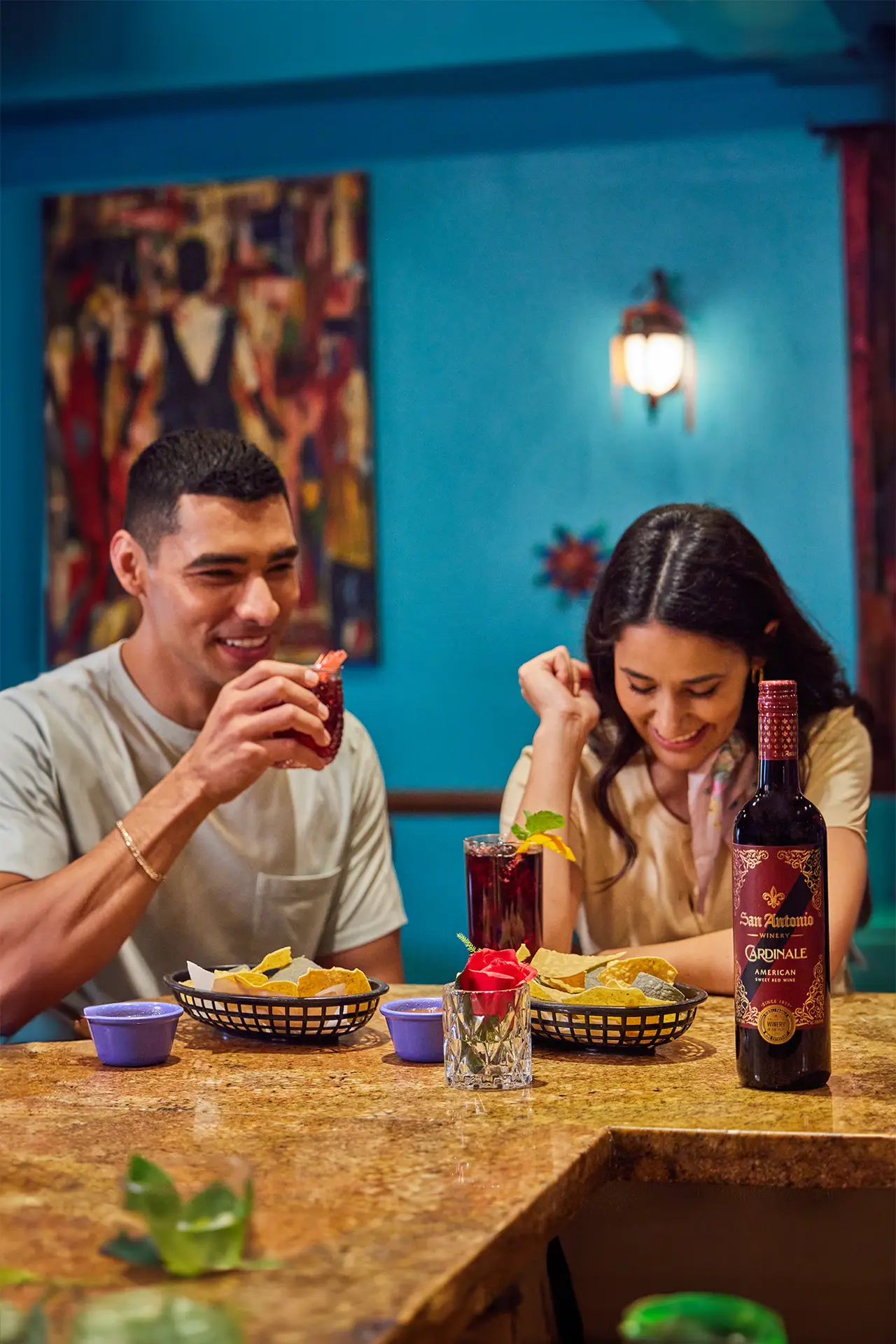 A couple enjoying drinks and snacks at a restaurant, with a bottle of San Antonio Winery Cardinale on the table.