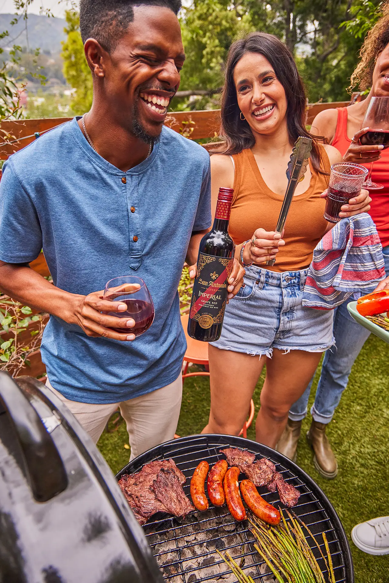 Friends laughing and holding San Antonio Winery Imperial wine at a backyard barbecue.