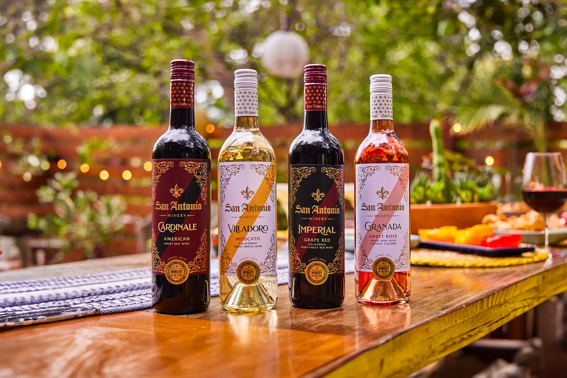 Four bottles of San Antonio Winery wines (Cardinale, Villadoro Moscato, Imperial, and Granada Sweet Rosé) on an outdoor table.
