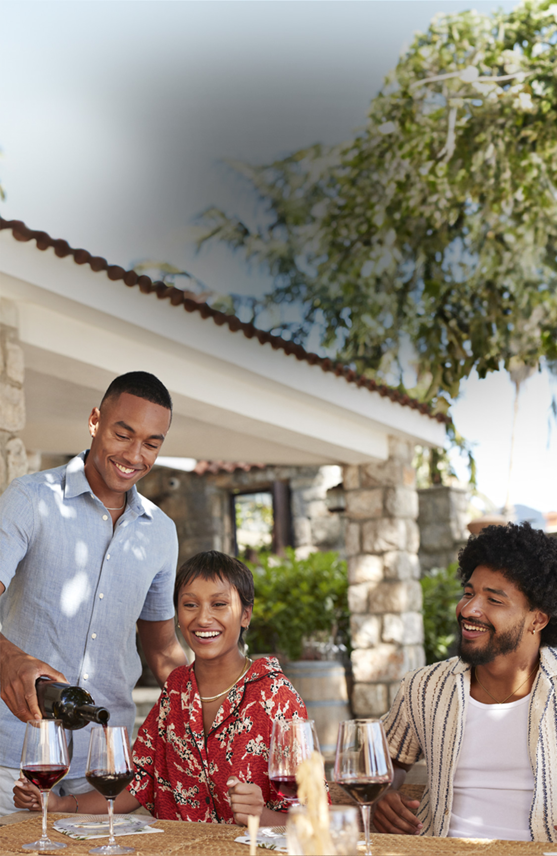 Three friends enjoying wine at an outdoor table, with one person pouring wine from a bottle of San Antonio Winery Port California sweet wine.